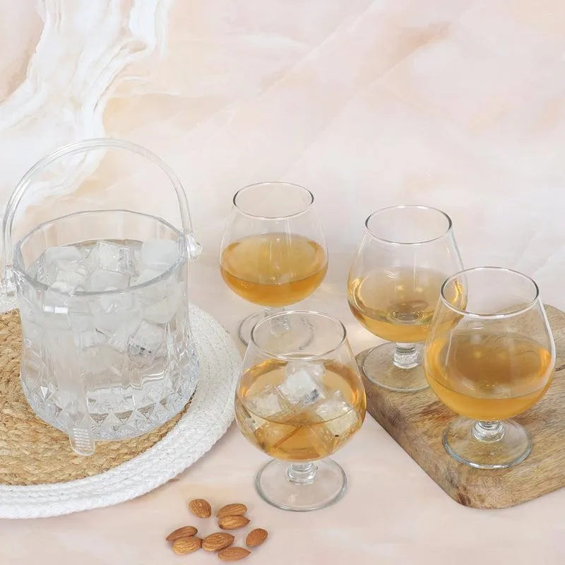 Transparent glass ice bucket with four snifter glasses arranged on a tabletop