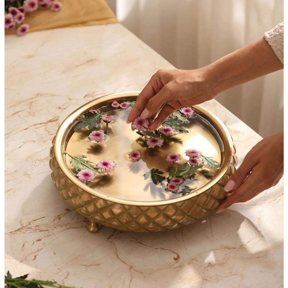 Hands placing flowers into the gold-toned decorative urli