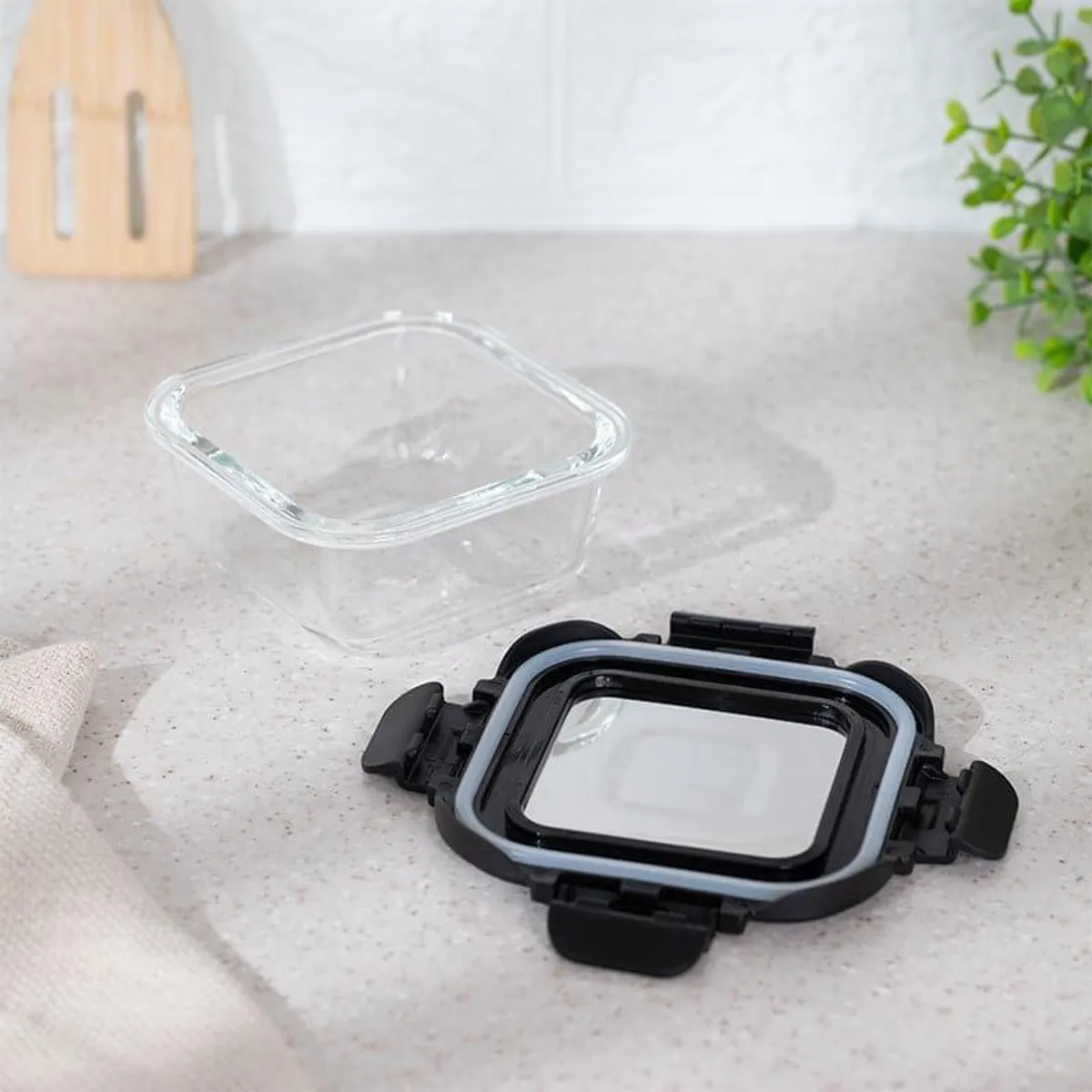 Clear square glass lunch box with its black lid and clips placed separately