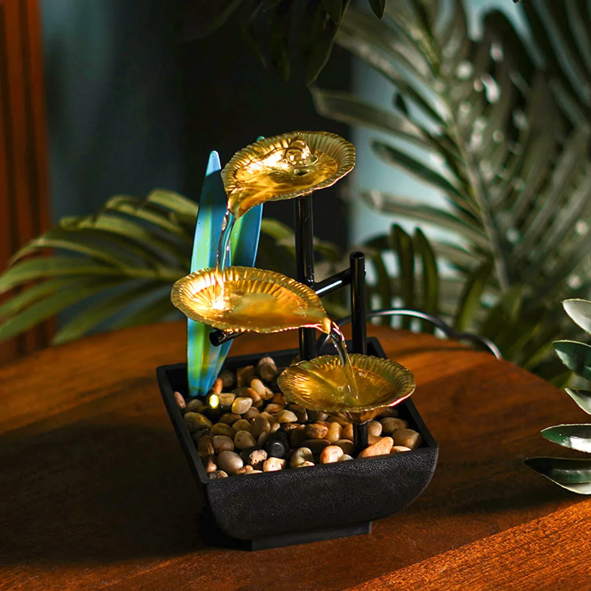 Gold tabletop fountain glowing among indoor plants on a wooden surface