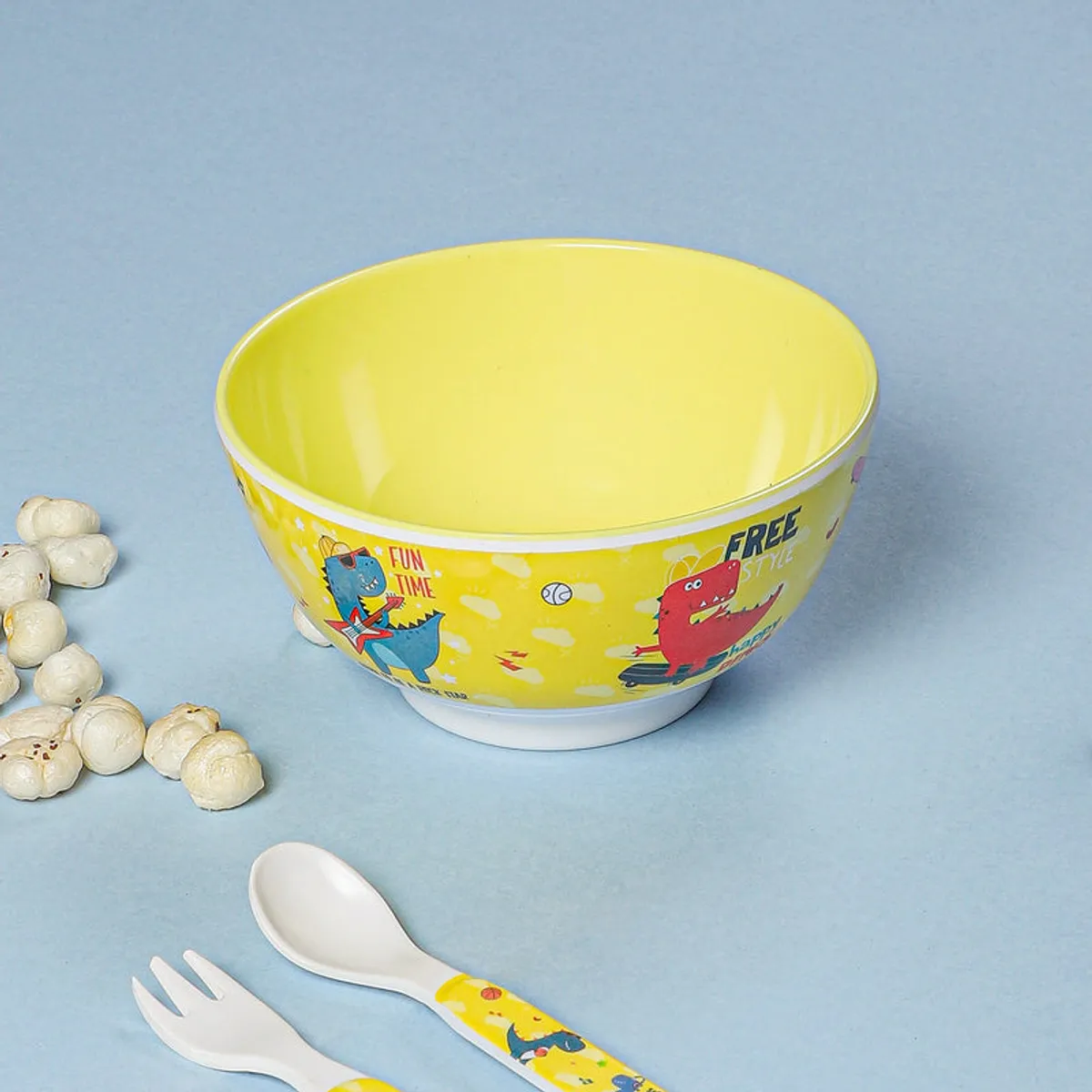 Yellow dinosaur-print snack bowl shown with popcorn and a spoon and fork.