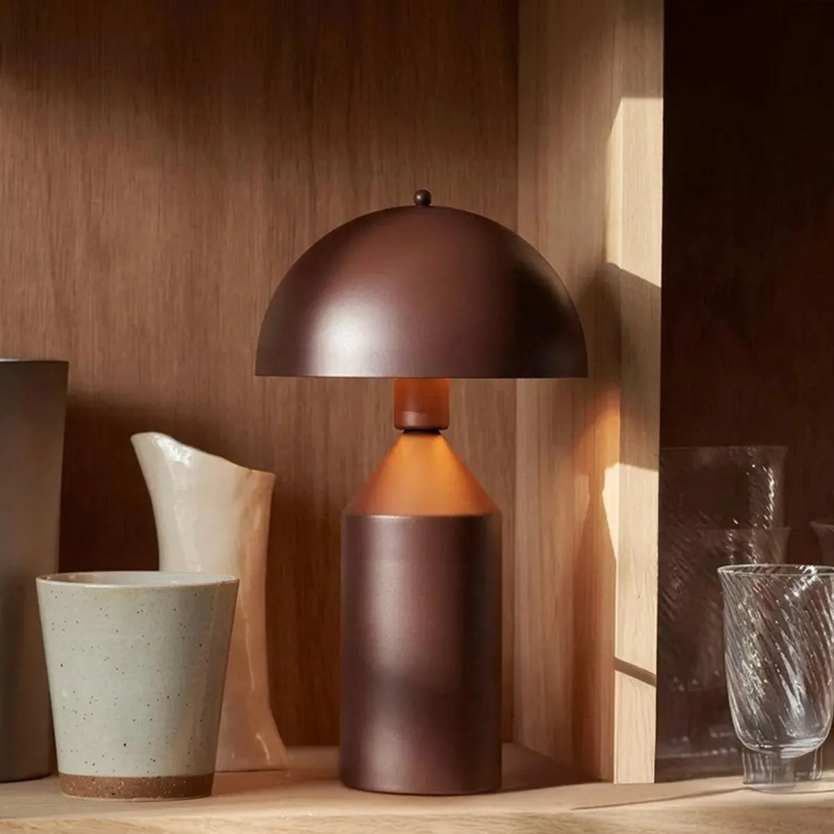 Brown metal lamp styled on a wooden shelf beside ceramic and glassware
