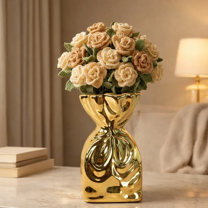 Gold sculptural vase holding beige crochet-style flowers on a tabletop