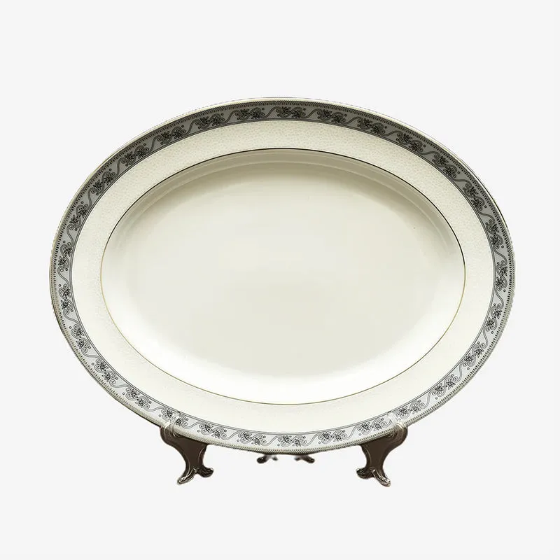 White porcelain oval platter with ornate floral border displayed on a stand.
