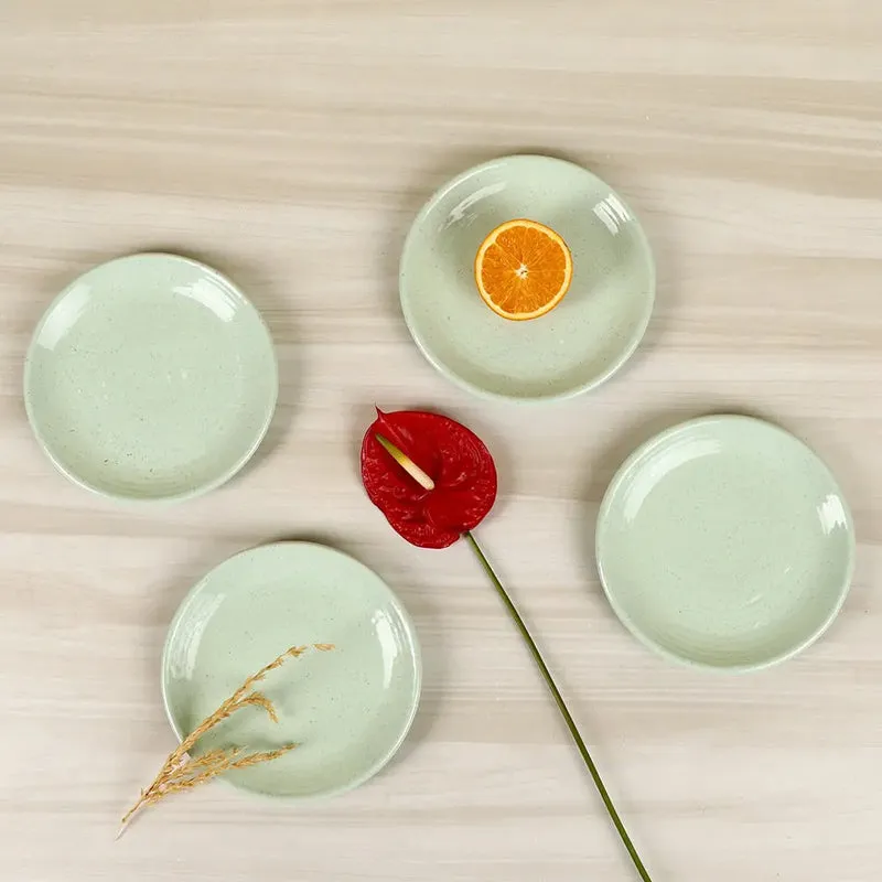 Four pale green ceramic quarter plates arranged on a light surface