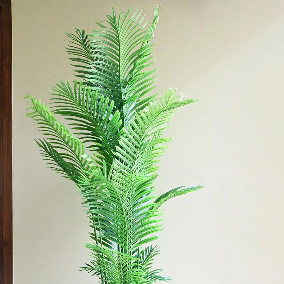 Green artificial palm fronds shown against a neutral wall