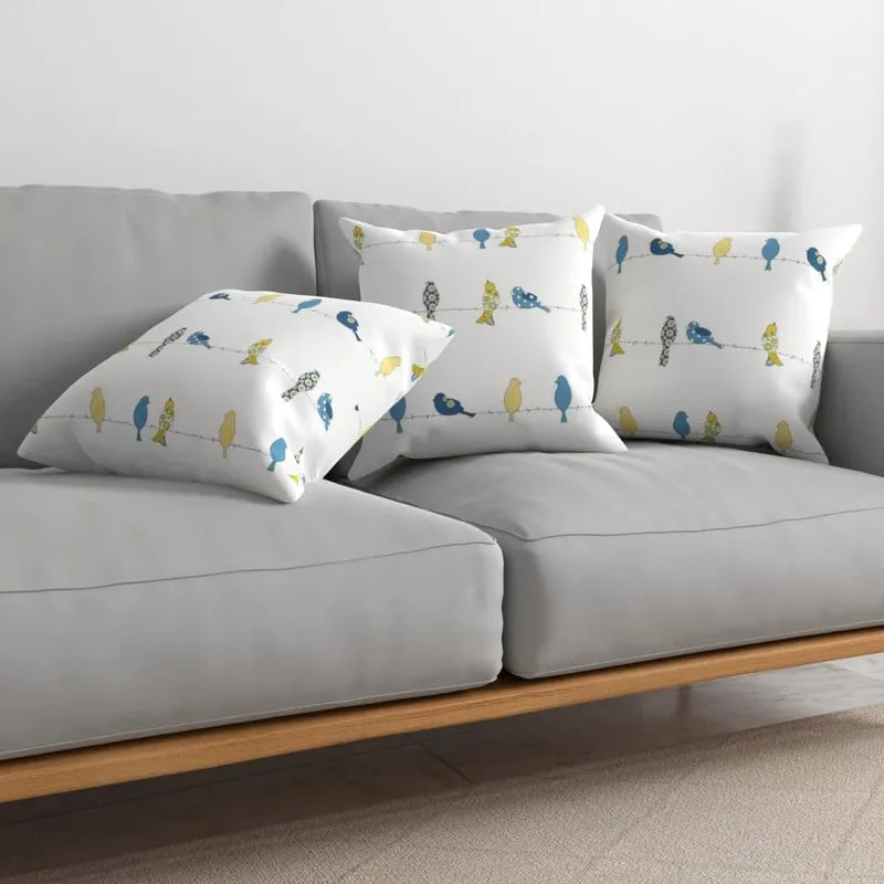 White cushion covers with blue and yellow bird motif on a grey sofa