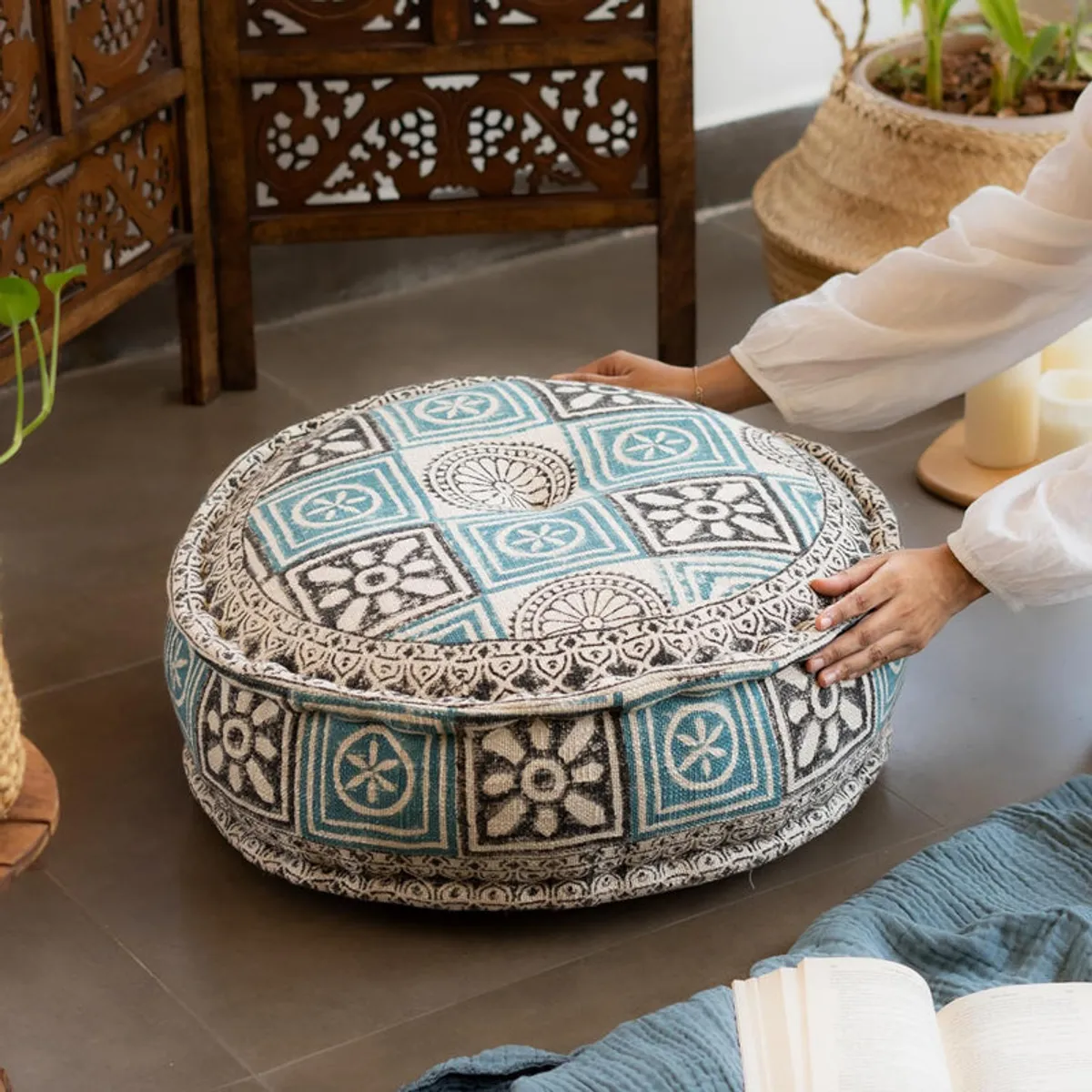 Person positioning a round blue and cream patterned floor cushion on the floor.