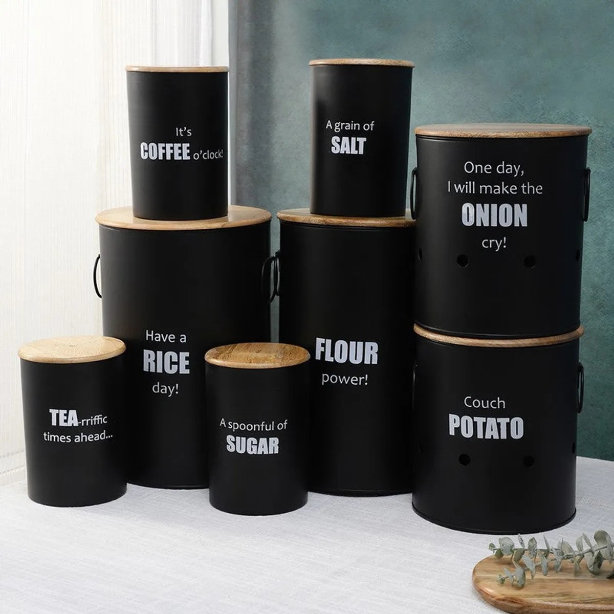 Black kitchen storage containers in varied sizes arranged against a light and teal backdrop.