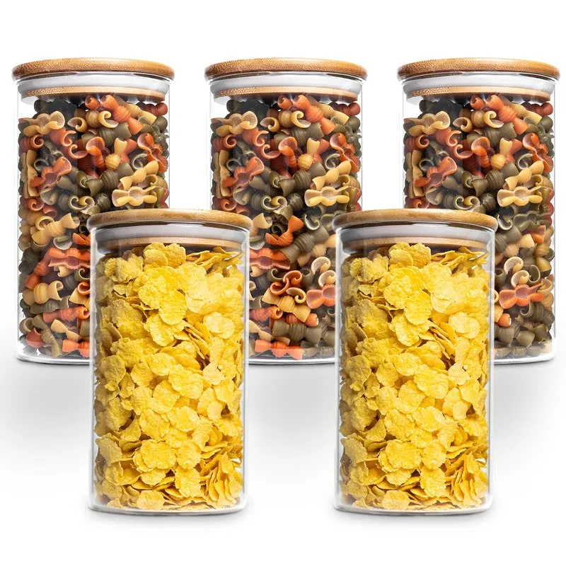Five transparent glass jars with bamboo lids filled with pasta and cereal.