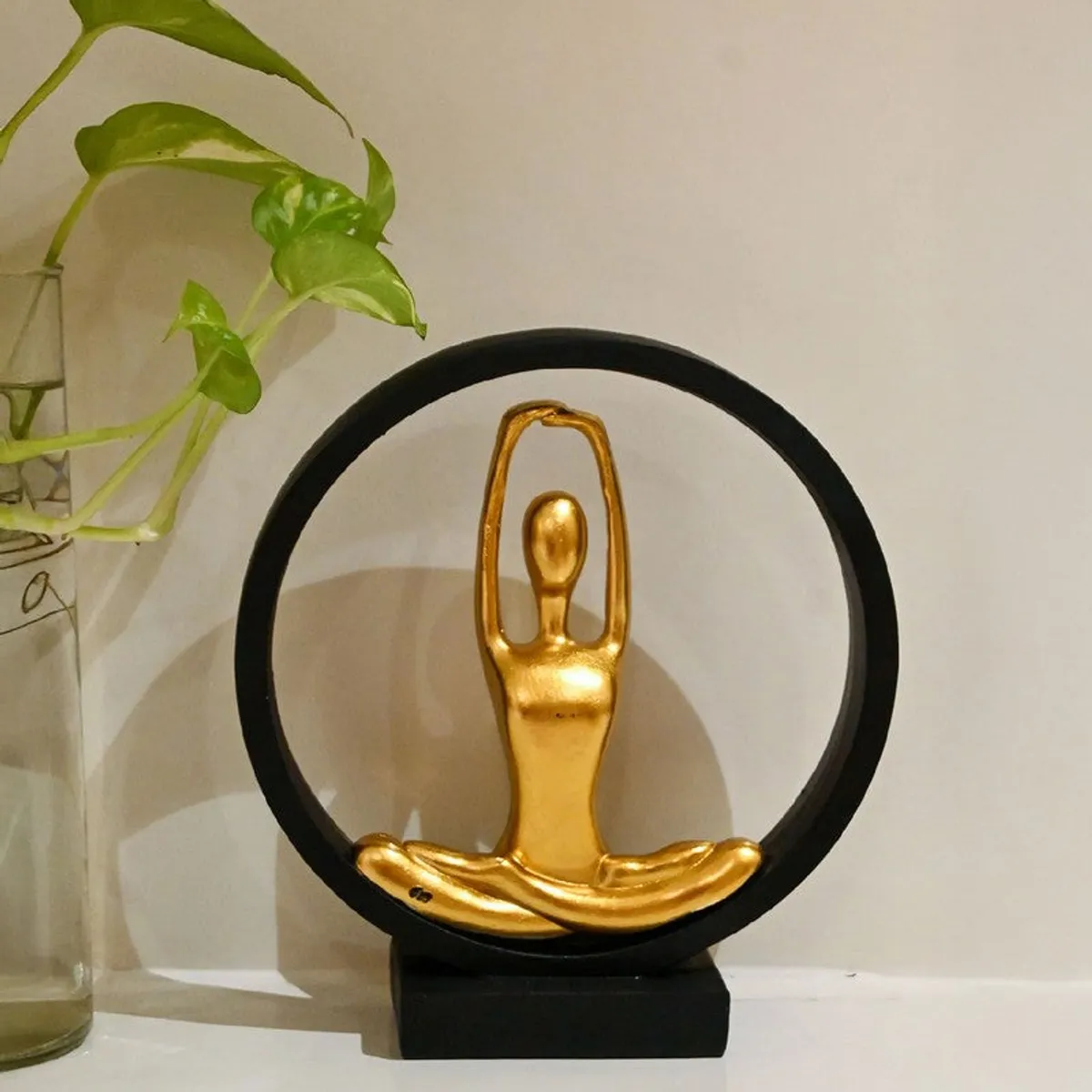 Black and gold yoga showpiece placed on a shelf beside a leafy plant