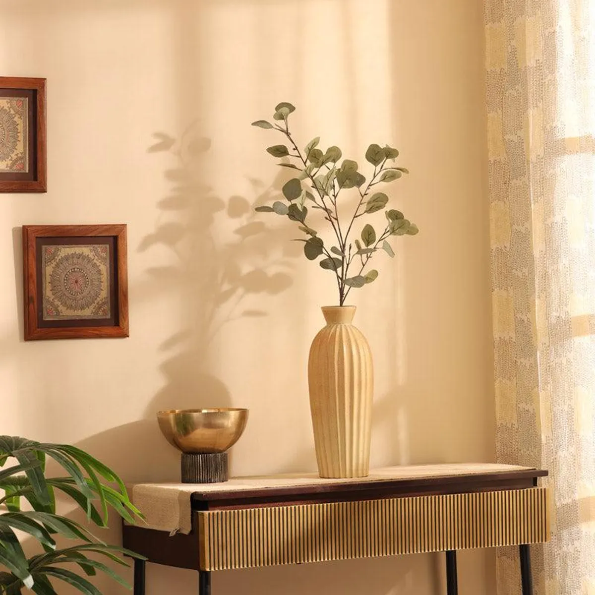 Green artificial eucalyptus stick styled in a tall vase on a console table