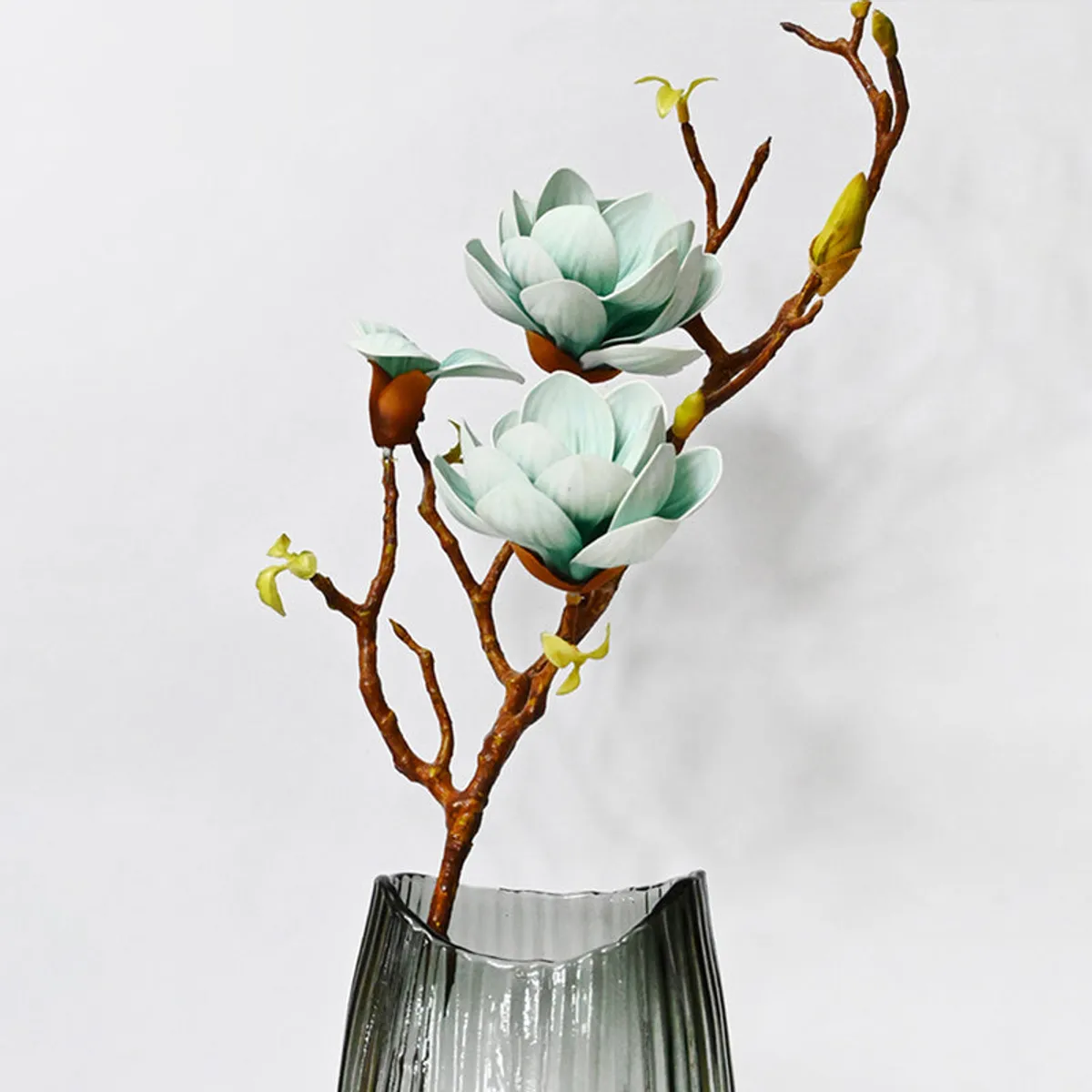 Artificial blue magnolia flower stick arranged in a clear vase.