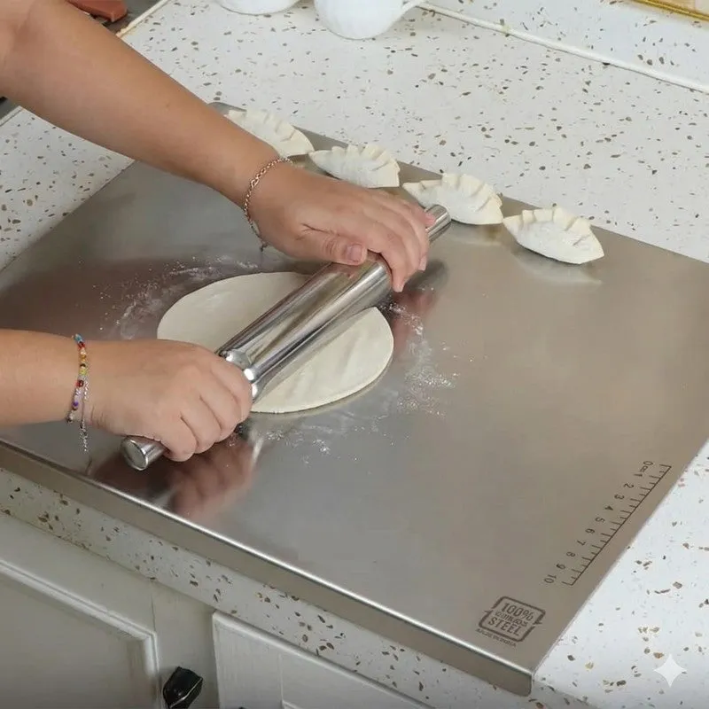 Hands rolling dough on a steel board with a steel rolling pin