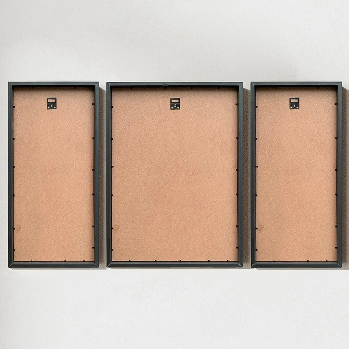 Back view of three black-framed wall art pieces with hanging hardware