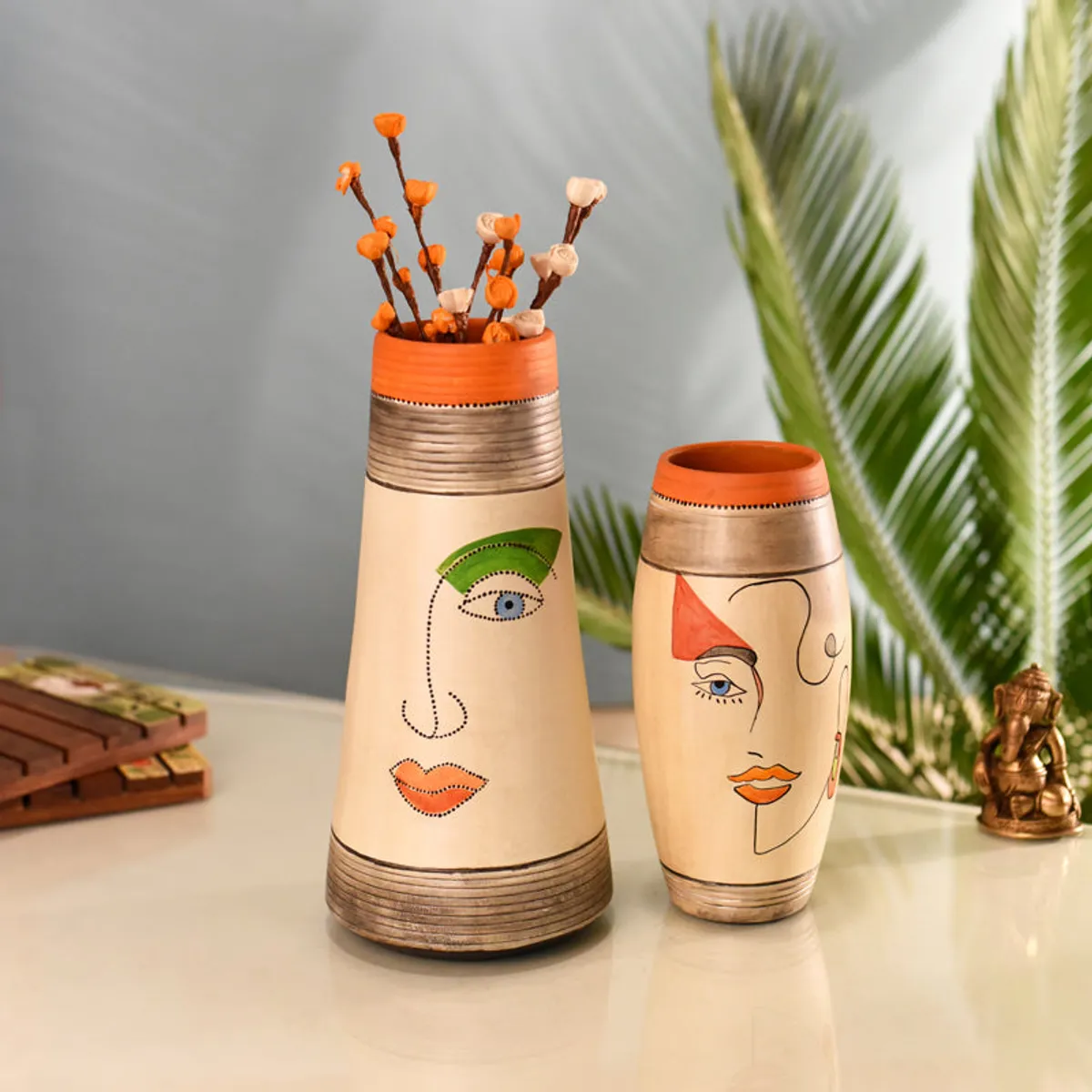 Set of two face-design vases on a tabletop with dried stems