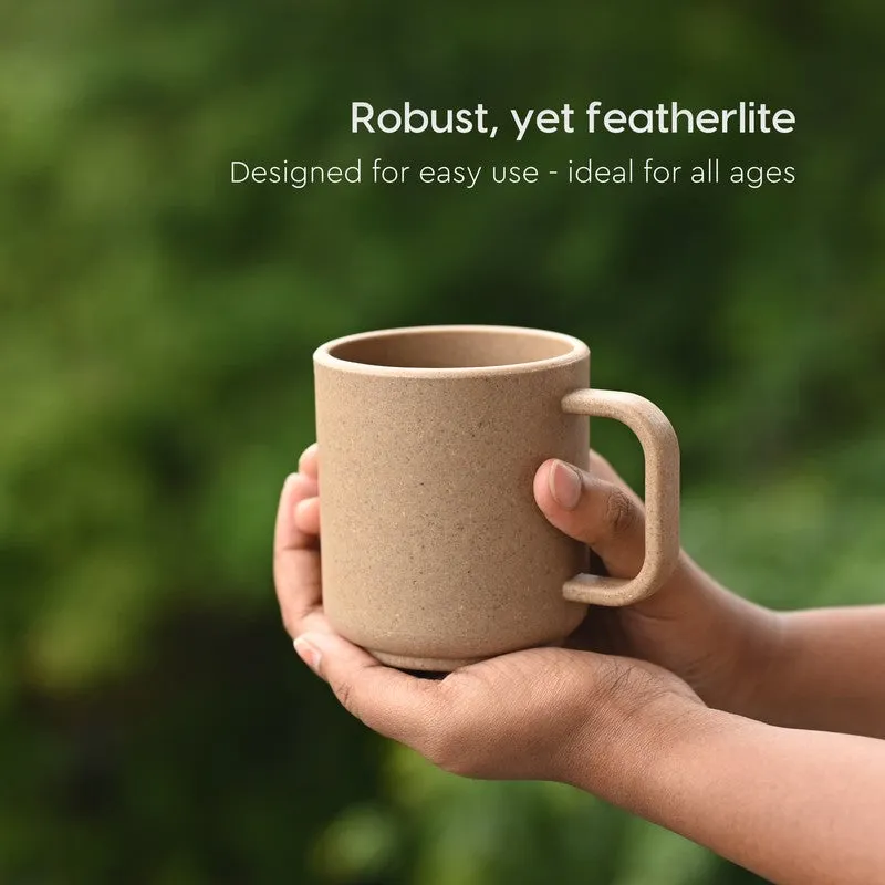 Brown mug held in both hands outdoors against a green background