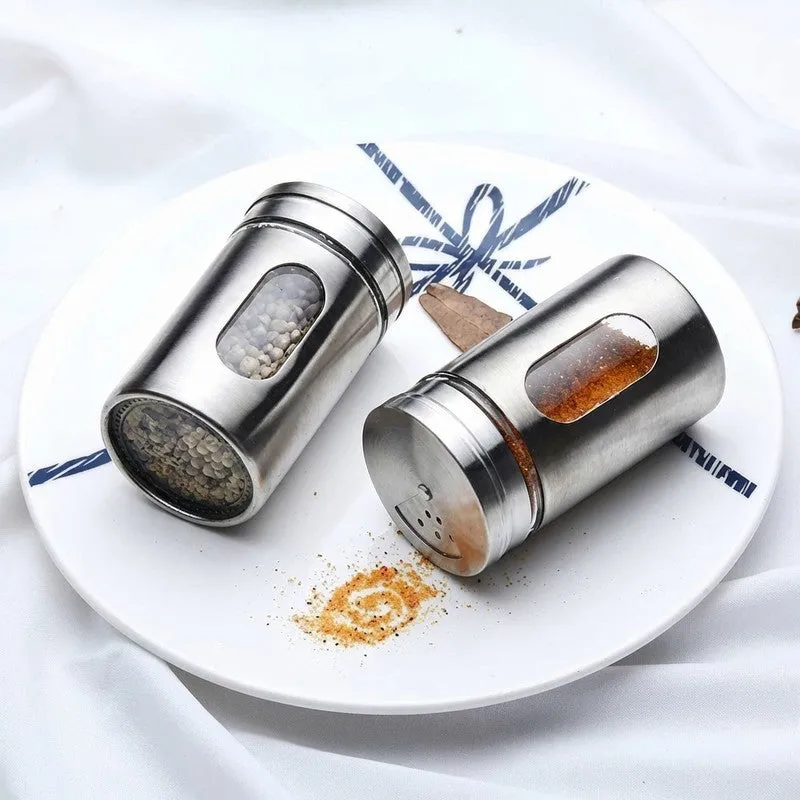 Two silver spice jars lying on a plate with spices visible inside.