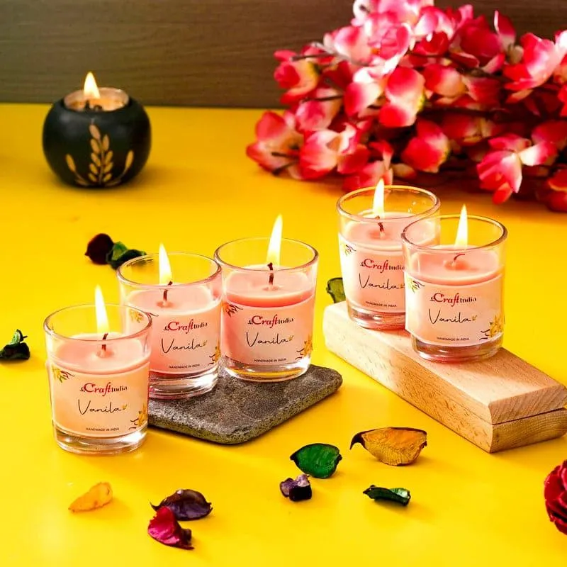Five orange votive candles arranged on colourful surfaces with flowers and scattered petals