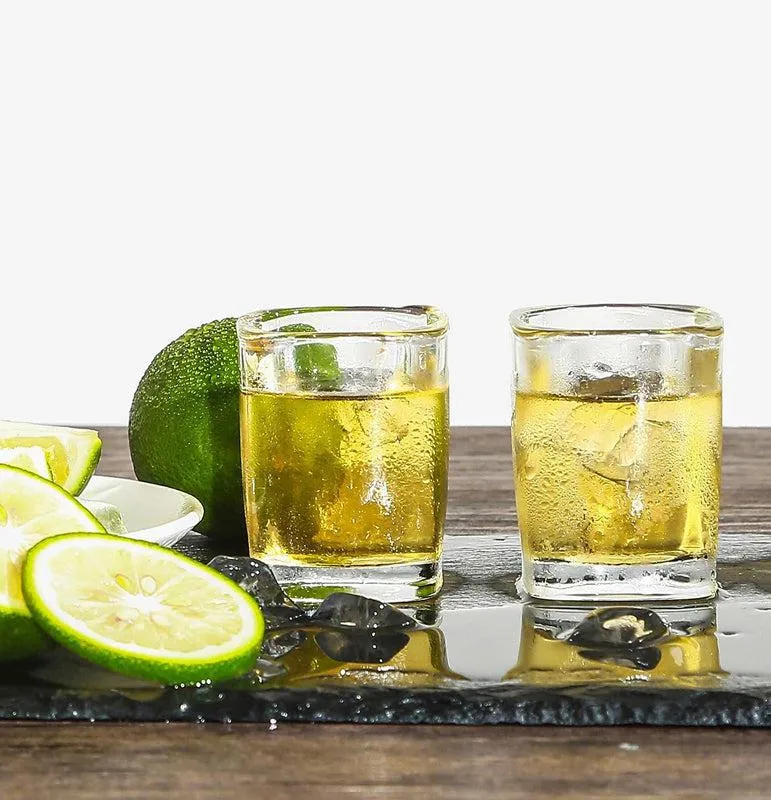 Two transparent square shot glasses with drinks on a dark serving surface