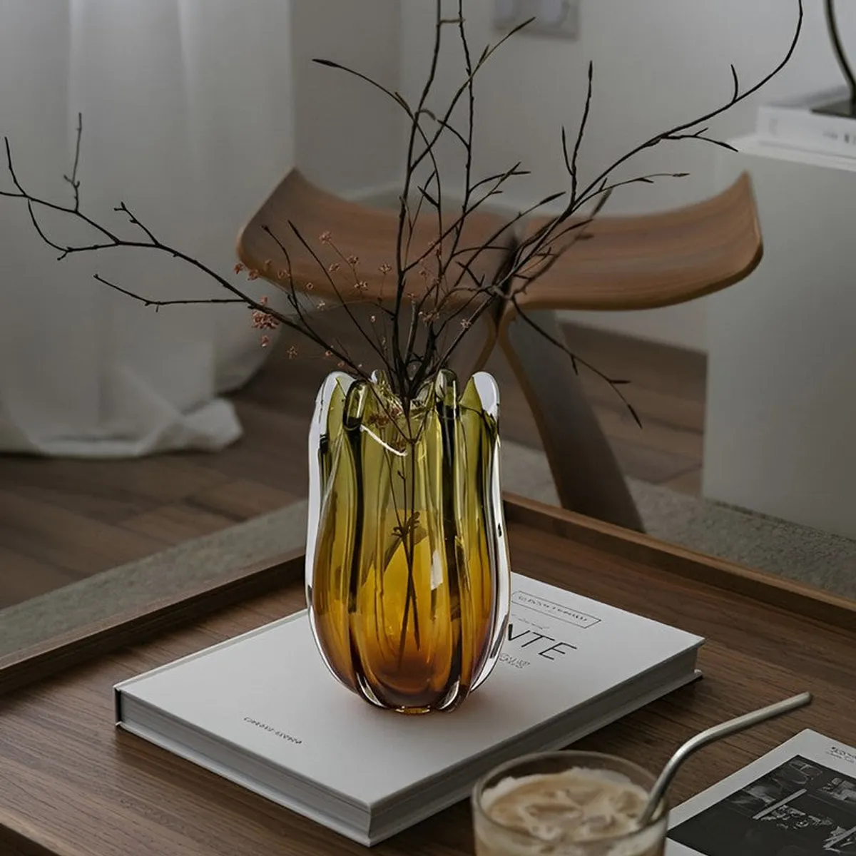 Green and gold ombre vase with branches placed on books on a wooden table.