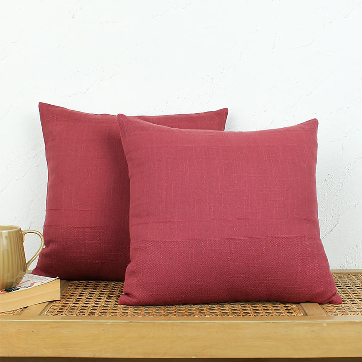 Two red square cushion covers arranged on a wooden bench beside a mug