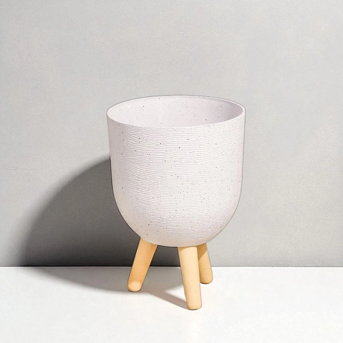 White textured planter with wooden legs against a softly lit neutral wall.
