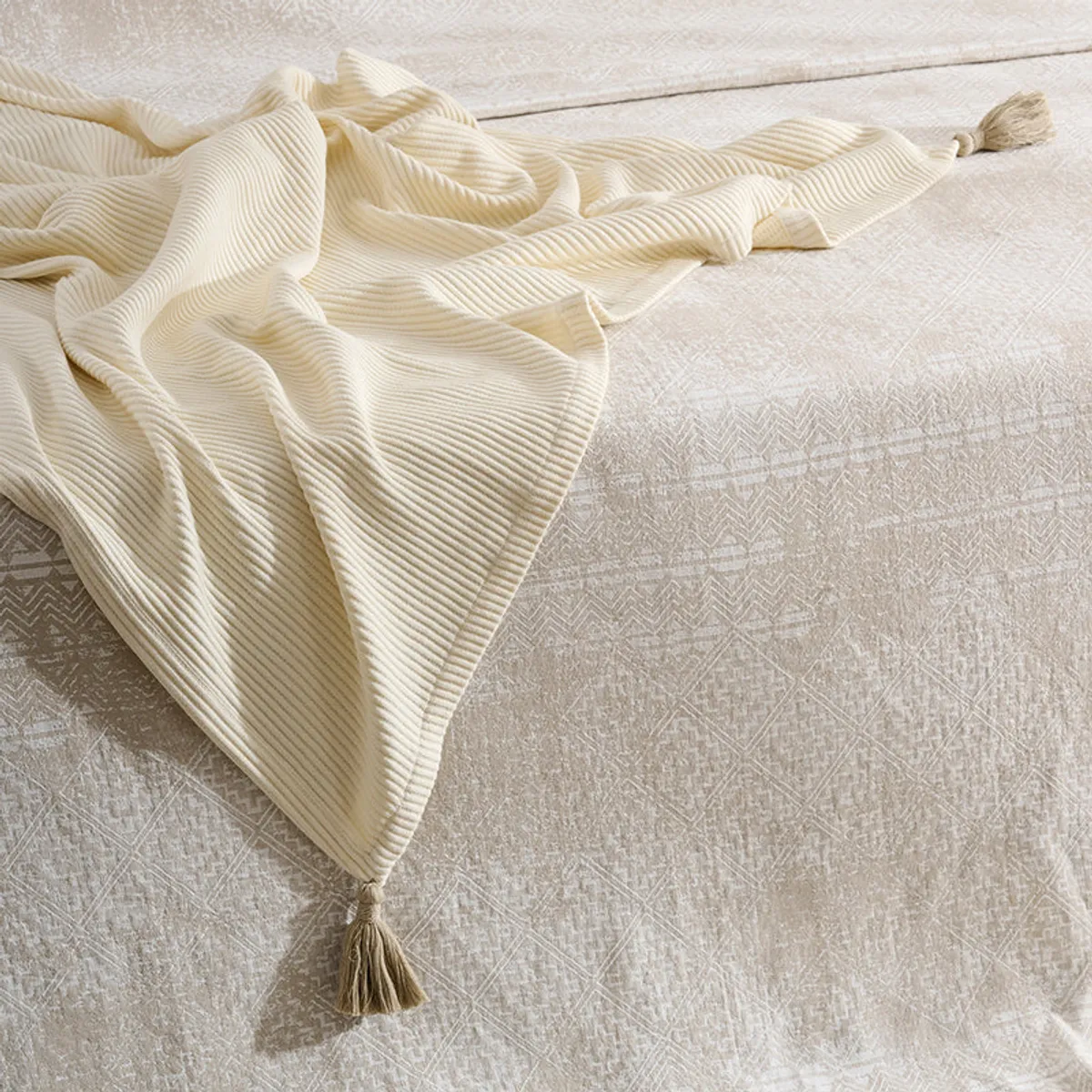 Ivory ribbed tasselled throw spread across a light patterned surface