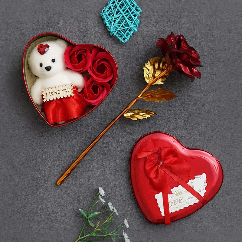 Heart-shaped red gift box with ribbon, teddy and red roses beside a decorative rose stem