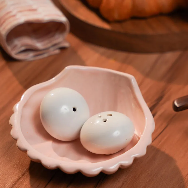 White salt and pepper shakers in a blush pink shell-shaped dish on a wooden table