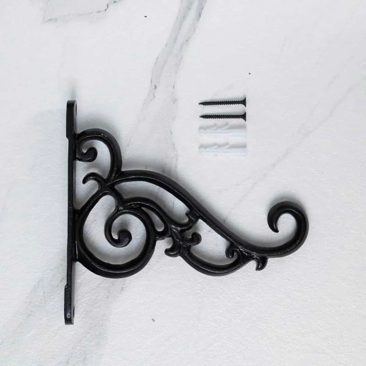 Black ornate wall bracket shown against a white wall with visible mounting holes.