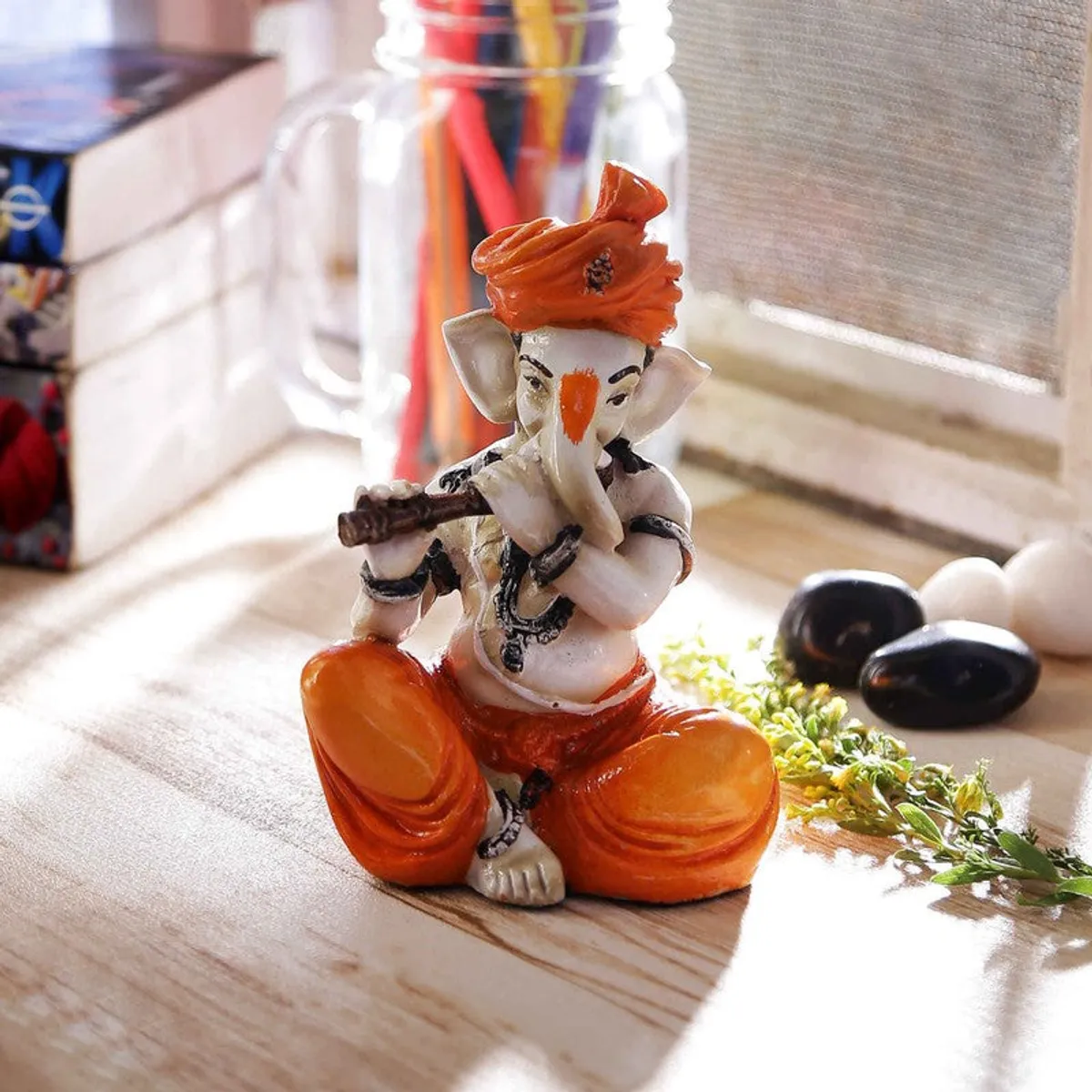 White and orange Ganesha resin showpiece placed near a window on a wooden surface