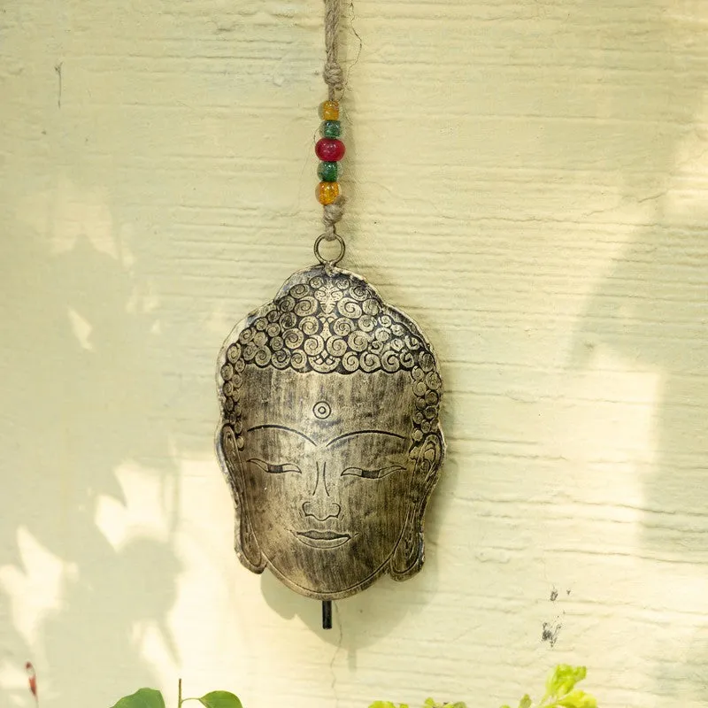 Gold Buddha-face hanging bell displayed against a sunlit wall