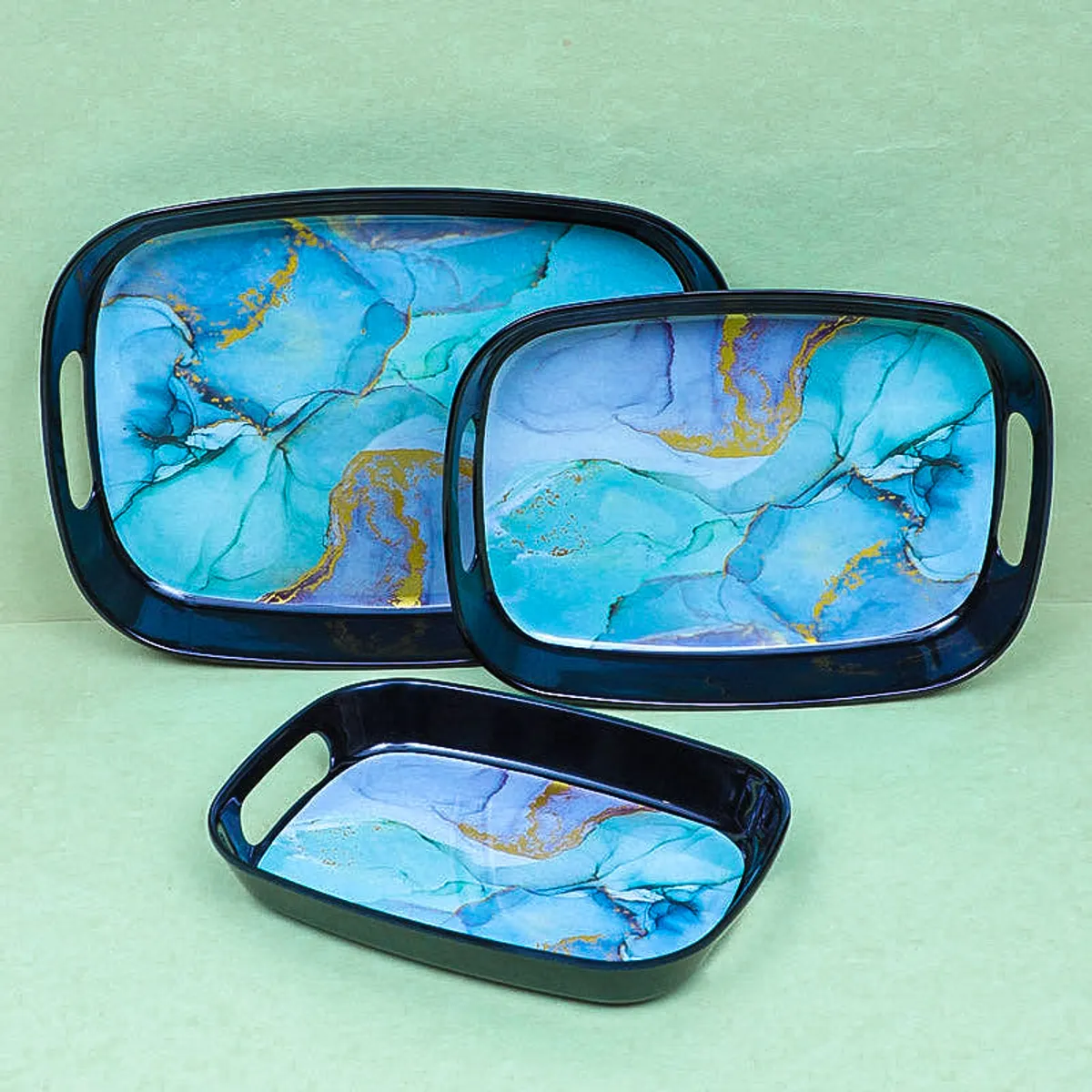 Three rectangular marbled serving trays arranged against a pale green backdrop