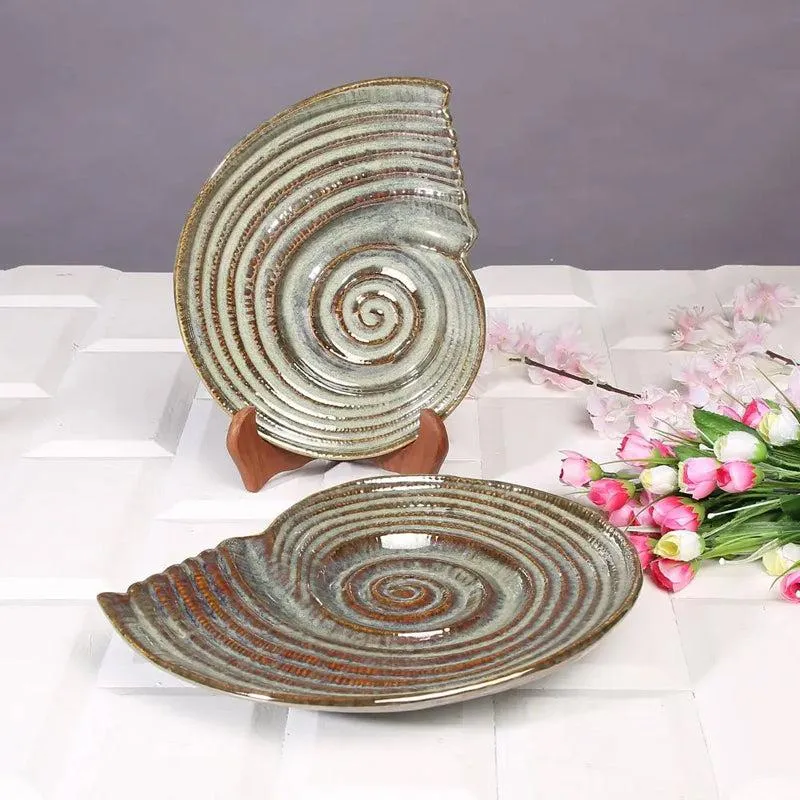 Glossy spiral ceramic platter shown upright and flat beside pink flowers