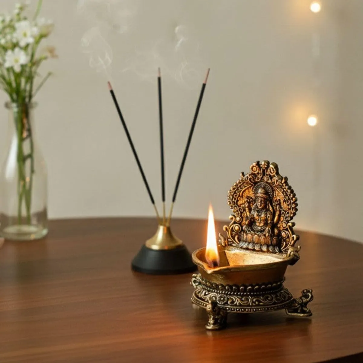 Lakshmi diya lit on a wooden surface beside incense sticks and a vase.