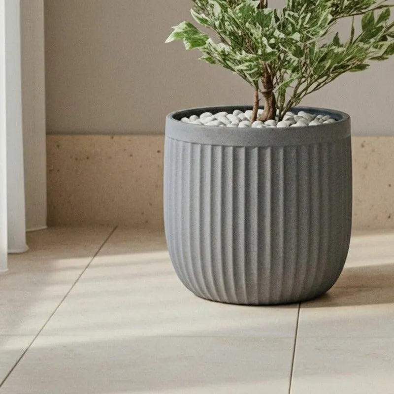 Grey ribbed planter with a leafy plant on a tiled floor.