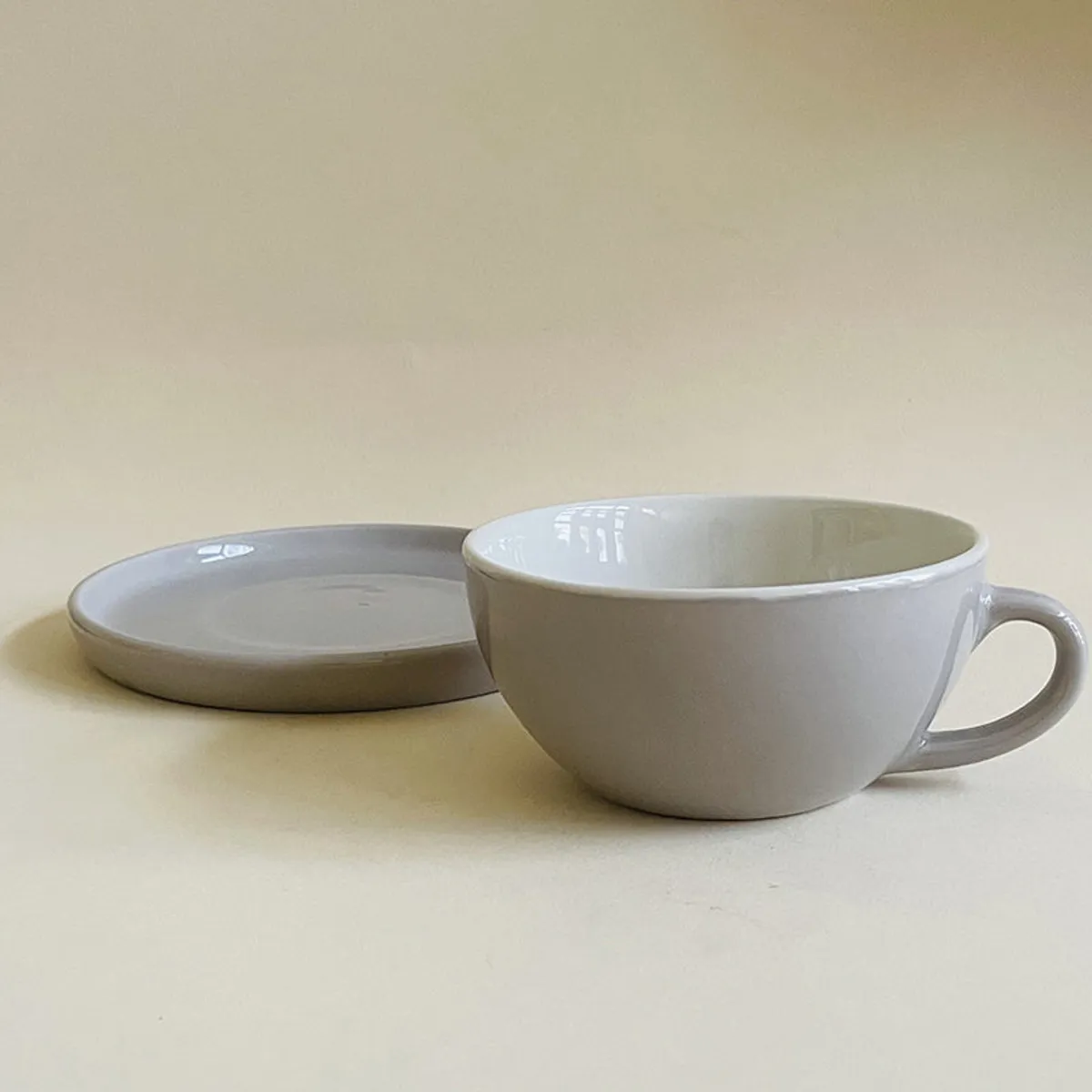 Single glossy grey cup beside its matching saucer on a neutral surface