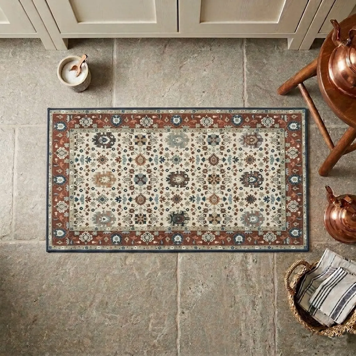 Ornate multicolour carpet placed on a stone floor near copper vessels