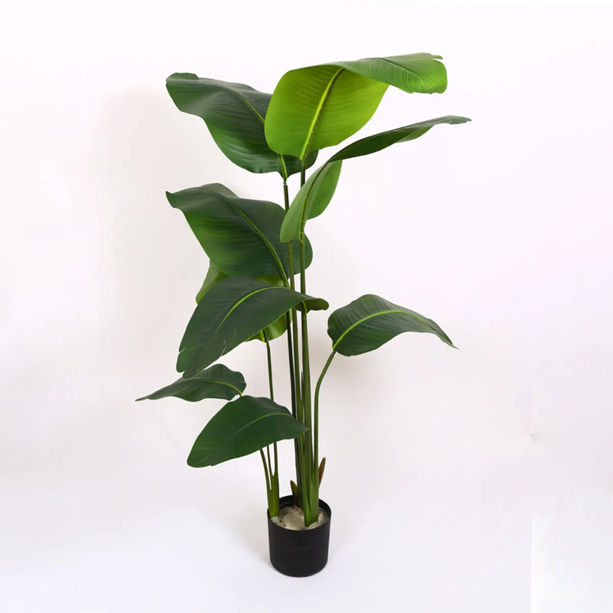 Artificial banana plant with layered green leaves in a black pot against a white background