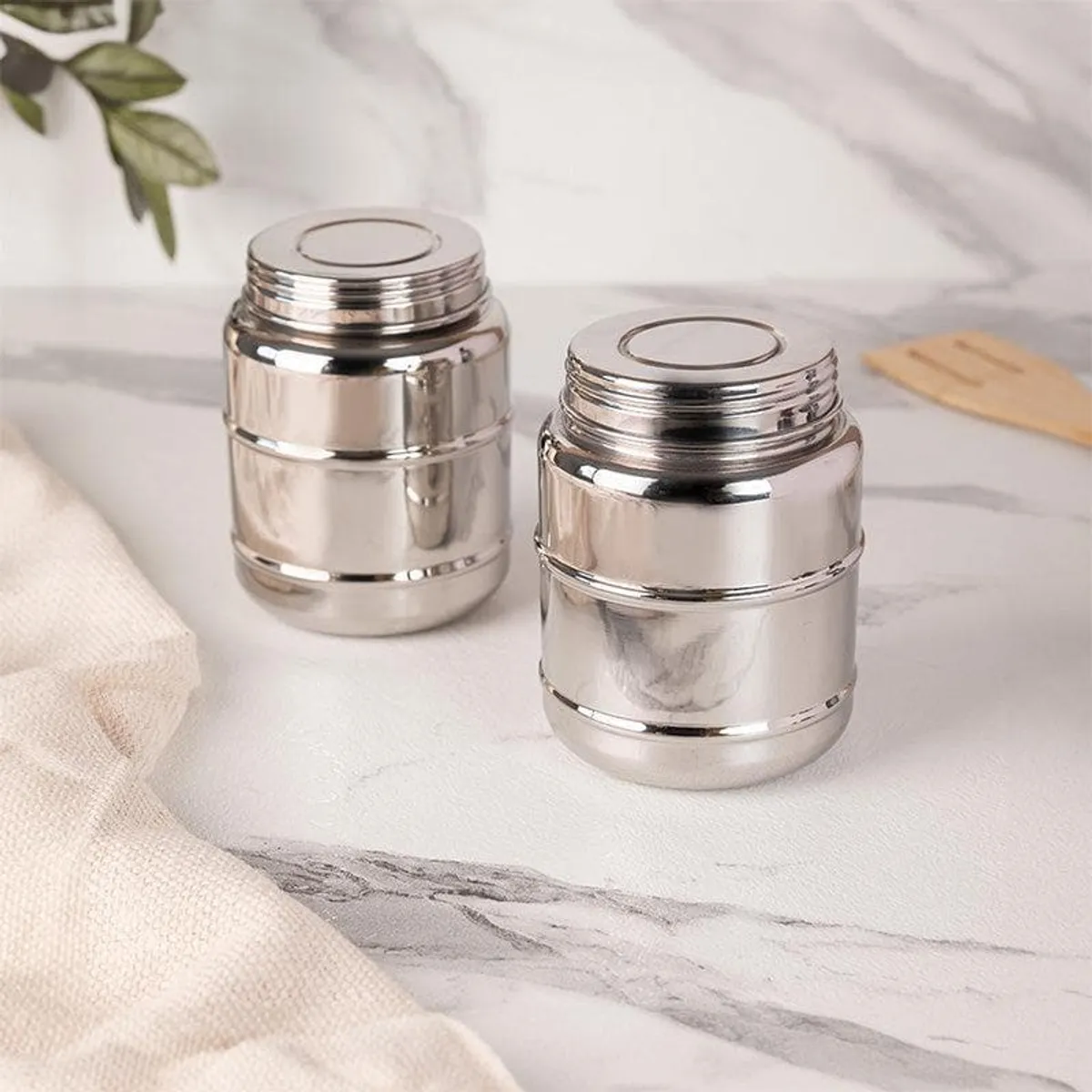 Two closed glossy silver storage containers displayed on a marble kitchen counter