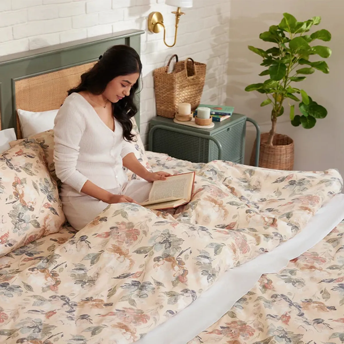 Person relaxing under beige floral bedding in a bright bedroom