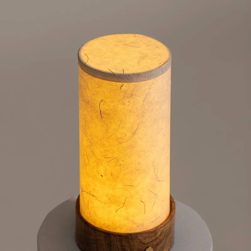 Lit ivory cylindrical lamp with warm glow and wooden base