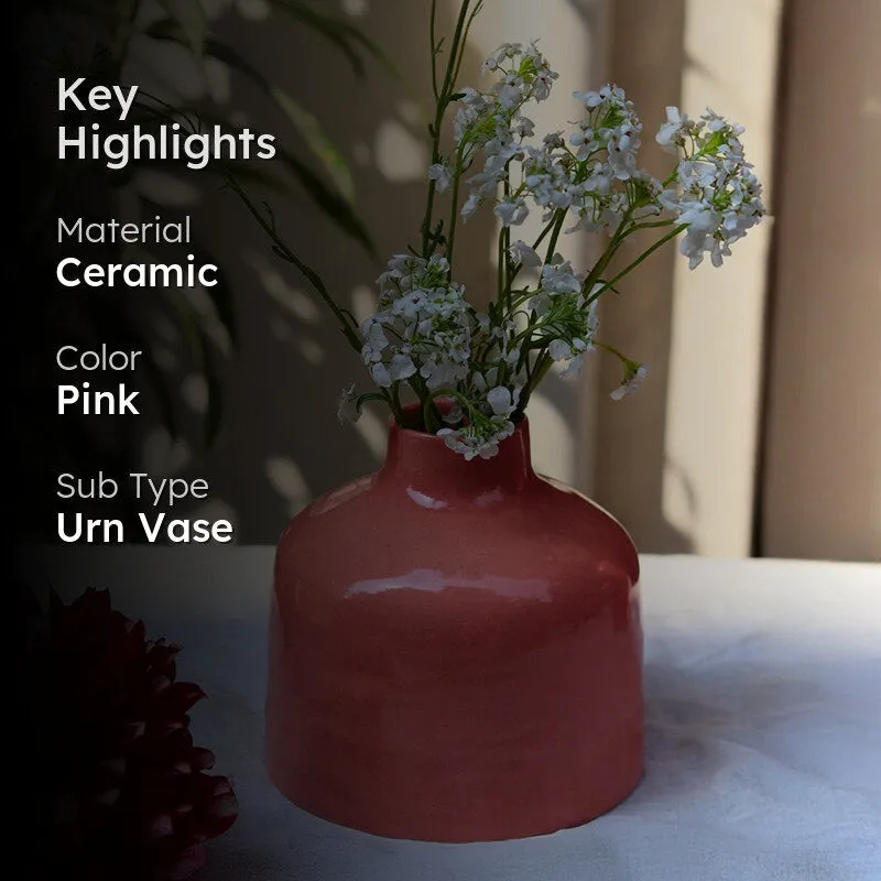Darkened lifestyle shot of a pink ceramic vase with white flowers on a table.