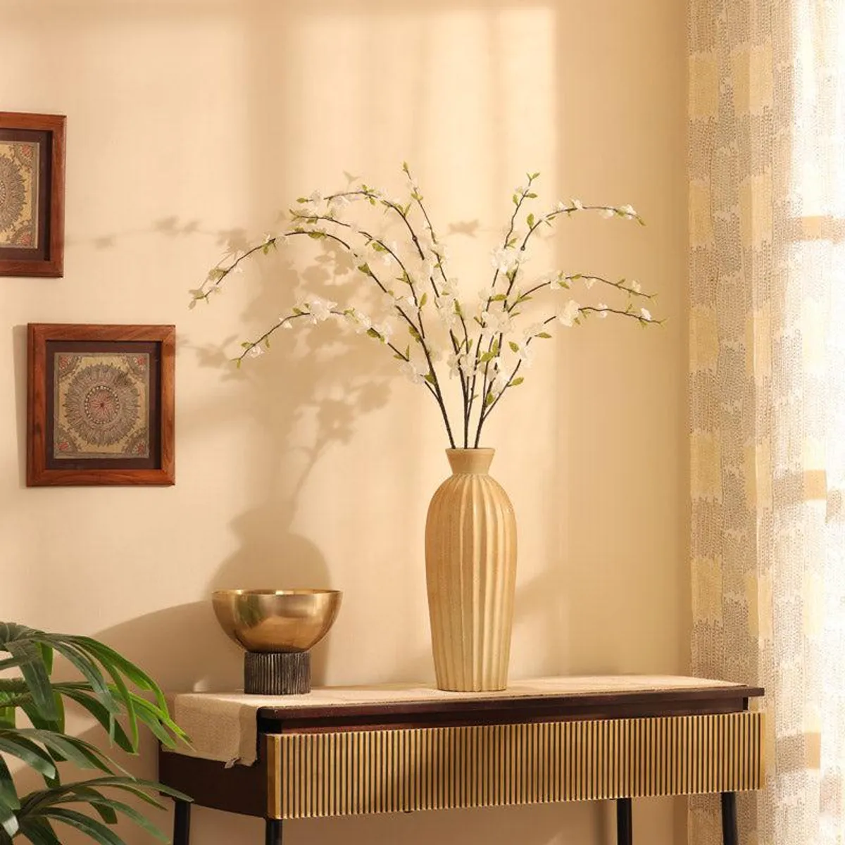 White cherry blossom flower sticks arranged in a tall beige vase on a console table