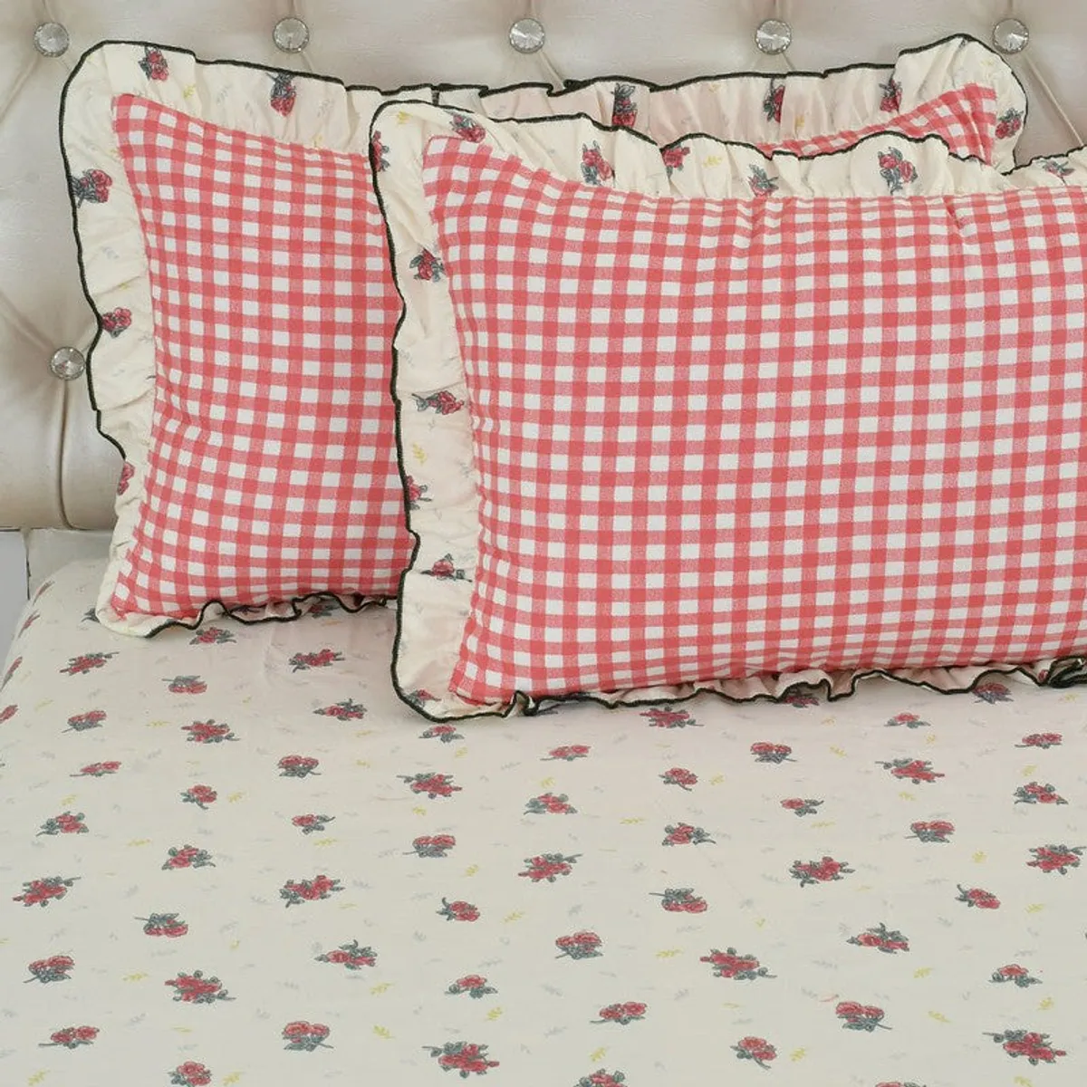 Two pink checked pillow covers with ruffled floral edges on off-white floral bedsheet