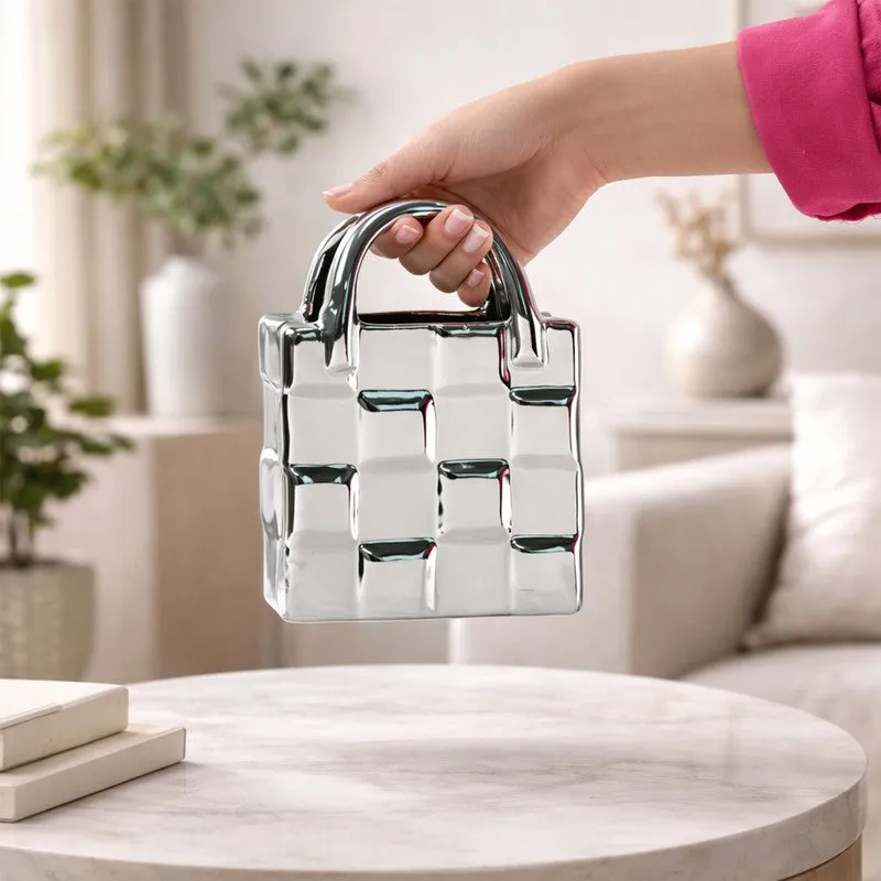 Hand holding a silver handbag-shaped vase above a round table