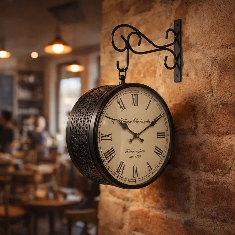 Vintage-style black wall clock with ornate floral sides mounted on a warm brick wall.