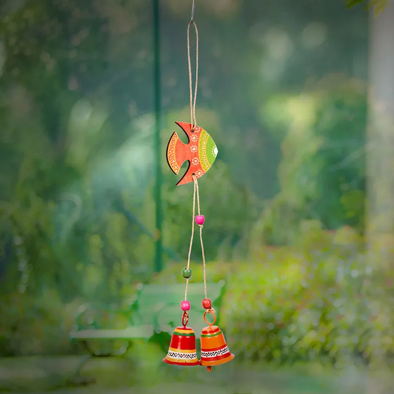 Orange and green fish-shaped windchime hanging outdoors with decorative bells.