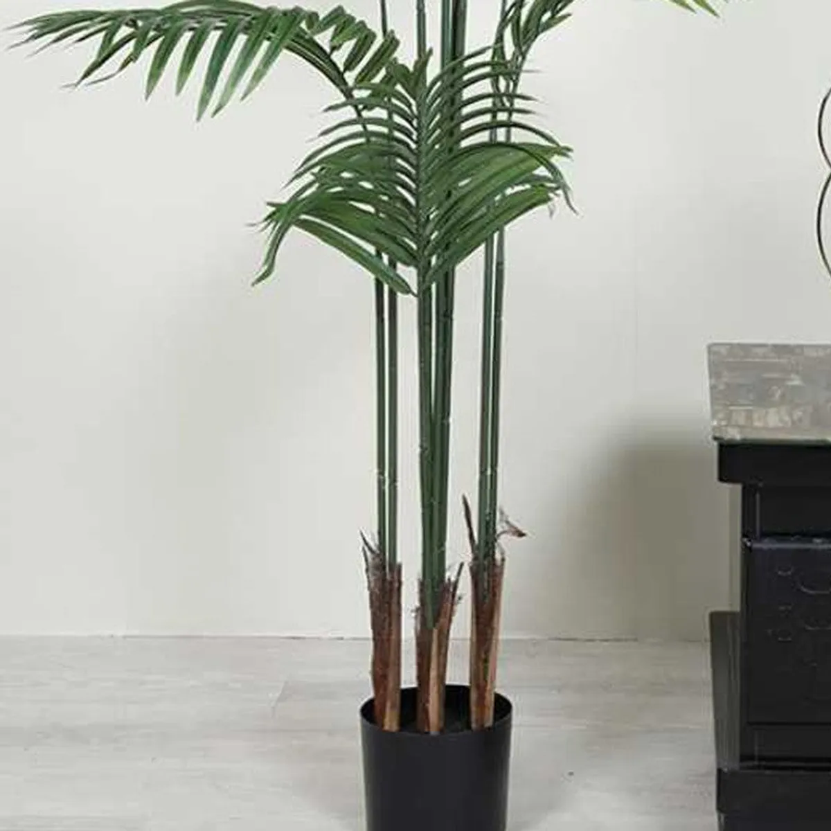 Close-up of green artificial palm fronds and brown stems above a black pot